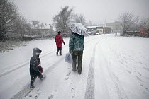 Family walking along road in snow, Denbigh, Denbighshire, Wales, January 2010