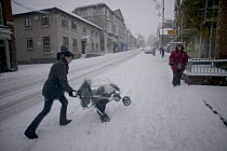 Mother struggling with pushchair in snow, Denbigh, Denbighshire, Wales, January 2010