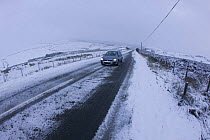 Car driving along moorland road in bad snow conditions, Denbigh Moor, Denbighshire, Wales, December 2009