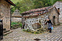 Old lady walking along sett-paved road in the isolated village of Bulnes, only accessible by cable car. Picos de Europa National Park, Cantabria, Spain. July 2008.