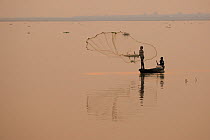 Silhouette of fisherman throwing net at sunset on the Dibru river, near Tinsukia, Assam, India March 2009