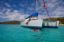Man diving off the bow of a Sunsail Lagoon 410 anchored in the BVI, into water close to a couple relaxing on a li-lo. April 2006, Model and property released.