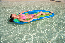 Woman relaxing on a lilo in the shallows. British Virgin Islands, March 2006. Model and property released.