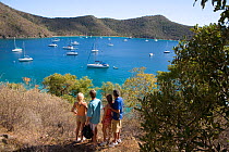 Friends walking in the British Virgin Islands, with yachts moored offshore, April 2006. Model released.