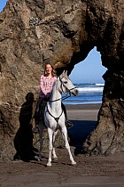 Arabian Horse and rider (Elicia) by rock archway on beach, northern California, USA (Model Released)