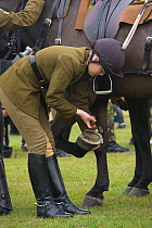 A soldier of the King's Troops, Royal Horse Artillery, dressed in training uniform, picks the feet of an Irish Draft horse before exercising in Wormwood Scrubs, London, UK. 2009