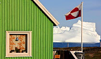 House in Qeqertarsuaq with the national flag flying, iceberg in distance, Qeqertarsuaq, Greenland, August 2009
