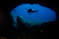 Two divers swimming past cave entrance, Deserta Grande, Desertas Islands, Madeira, Portugal, August 2009