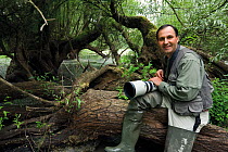 Photographer, Elio della Ferrera, holding camera sitting on fallen tree, in an oxbow of the Sava river flooded area, Lonjsko Polje Nature Park, on the Croatia Bosnia and Herzegovina border, June 2009