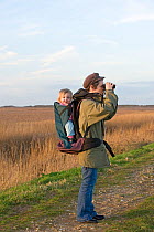 Mother carrying toddler in backpack while bird watching along coastal path, North Norfolk, UK, January 2008, model released