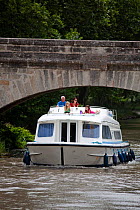 Family cruising under a bridge on the Canal Du Midi near Capestang, Languedoc, France. July 2009. Model and property released.