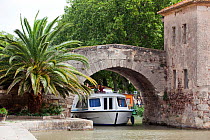 Boat passing under a bridge on the Canal Du Midi, Le Somail, France. July 2009. Model released.