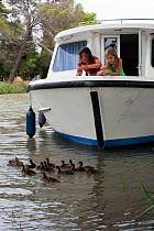 Girls feeding mallard ducks from the bow of a boat, cruising on the Canal Du Midi near Capestang, southern France. July 2009. Model and property released.