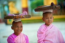 Two young Buddhist girl nuns wearing pink robes, carrying items on their heads, Bago, Myanmar, Burma. August 2009