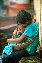 Two children, one sheltering the other, in heavy rain, during the monsoon, Bago, Myanmar, before Burma.  August 2009