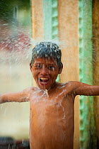 Boy playing in heavy monsoon rain, during the raining season, Bago, Myanmar, Burma.  August 2009