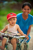 Portrait of a young boy, sat on the handlebars of a bicycle, with his mother behind him,Inle Lake area, Shan State, Myanmar, Burma  August 2009