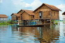 Fisherman rowing his boat, past a row of floating houses in the waters of Inle Lake, Shan State, Myanmar, Burma. August 2009