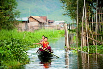 Two young boys in a traditional boat,  rowing up a river, Inle Lake, Shan State, Myanmar, Burma. August 2009