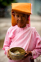 Portrait of an elderly Buddhist nun holding a donations bowl, Mandalay, Mandalay Division, Myanmar, Burma. August 2009