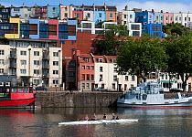 Rowers on Bristol's floating harbour, with colourful town houses and apartments in the background. England, UK, 2009.
