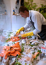 Fishmonger selecting fish for a customer from a window display, Bristol, England, UK, 2009. Model/property released.