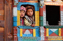Two children looking through decorated window of traditional building. Tamang ethnic group, Tamang heritage trail, Gadlang, Langtang region, Nepal. November 2009