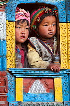 Two children looking through decorated window of traditional building. Tamang ethnic group, Tamang heritage trail, Gadlang, Langtang region, Nepal. November 2009
