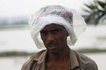 Man sheltering under plastic hat in monsoon rain, Ganges delta, Bangladesh, November 2008
