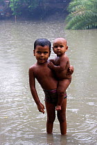 Young Bangladeshi child holding young brother in monsoon rain washing in pond, Ganges delta, Bangladesh, December 2008