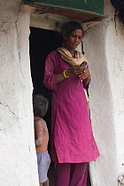 Woman standing in doorway using mobile phone at her home in industrial slum, Bhopal, Madhya Pradesh, India, November 2008