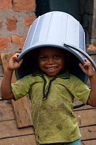 Young boy playing with plastic bucket in industrial slum, Bhopal, Madhya Pradesh, India, November 2008