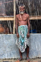 Man standing outside building in pouring rain, Ganges delta, Bangladesh, November 2008