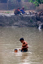 Father, baby and son washing in village pond during the monsoon rain, Ganges delta, Bangladesh, November 2008