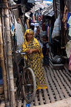 Woman walking through narrow alleyway between buildings in slum, Dhaka, Bangladesh, November 2008