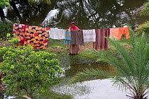 Woman hanging out washing in waterlogged garden, waterlogging caused by siltation of rivers, Bangladesh, November 2008