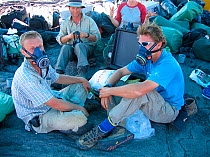 Film crew wearing gas masks to protect themselves from the poisonous gases given off by the mineral deposits, sitting on laval field of Erta Ale volcano, The Rift Valley, Ethiopia, November 2003, Film...