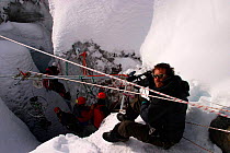 Chadden Hunter (cameraman) filming inside a moulin, the ice chute that drains meltwater through glaciers; camera equipment secured using ropes, scaffolding poles and bicycle wheels, for the Mountains...