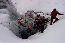 Film crew hanging on ropes inside a moulin, ice chute that drains meltwater through glacier, using ropes, scaffold poles and bicycle wheels to secure cameras, for the Mountains Episode of the BBC tv s...