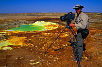 Cameraman, Martyn Colbeck, filming the Dallol hot springs where water heated by magma laden with potassium, sulphur and iron spews up through salt pans staining the salt deposits with vivid colours, i...