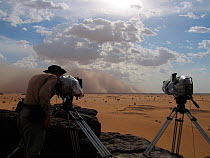 Cameraman, Justin Maguire, makes final adjustments to two timelapse cameras protected by thick plastic covers as a sandstorm approaches at 80km/hour, for the Deserts Episode of the BBC tv series Plane...