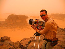 Cameraman, Justin Maguire, wearing protective goggles filming in a Saharan sandstorm, for the Deserts Episode of the BBC tv series Planet Earth, Sahara desert, northern Niger, June 2005