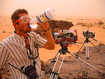 Director, Chadden Hunter, drinking water to wash the sand out of his mouth, in a Saharan sandstorm. Two timelapse film cameras are protected by thick plastic jackets, for the Deserts Episode of the BB...