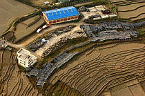 Aerial view of building with buildings supplies surrounded by terraced fields, Himalayan foothills, Nepal, December 2007