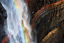 Rainbow in Hengifoss waterfall flowing over layers of grey basalt and reddish sandy clay, Iceland, August 2008