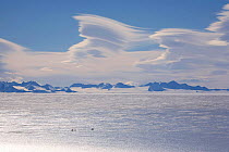 Two snowmobiles on the blue ice in front of the Ellsworth Mountains, with orographic clouds above. Antarctica, January 2006.