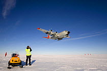 C130 equipped with skis flying over groomed skiway prior to landing, man and ski mobile in foreground. Patriot Hills, Antarctica, January 2006.