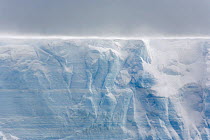 The top of a large tabular iceberg shines with the backlit snow blowing along the surface in windy weather. Antarctica, October 2006.