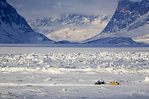 Inuit hunter travelling by snowmobile through tidal ice in Pangnirtung Fiord. Nunavut, Canada, , April 2008.