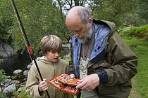 Man and boy select a fly from a fly box whilst fishing for Salmon on the River Findhorn. Scotland, UK, September 2007.